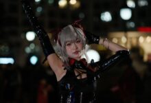 A cosplayer in detailed costume poses confidently in a lively night scene.