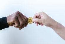 Two hands exchanging a Bitcoin coin, symbolizing cryptocurrency transactions.