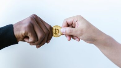 Two hands exchanging a Bitcoin coin, symbolizing cryptocurrency transactions.