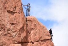 Two climbers ascending red sandstone cliffs on a clear day.