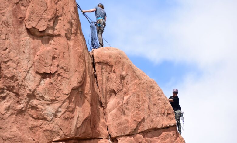 Two climbers ascending red sandstone cliffs on a clear day.