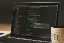 A close-up of a laptop displaying code in a dimly lit room with a coffee mug nearby.