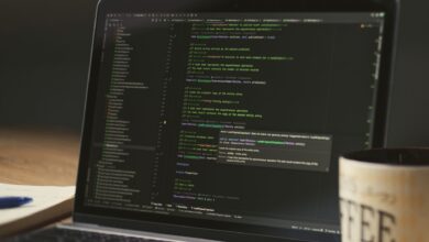 A close-up of a laptop displaying code in a dimly lit room with a coffee mug nearby.