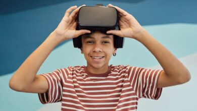 Cheerful little boy in t shirt putting pn VR glasses and looking at camera against blue wall