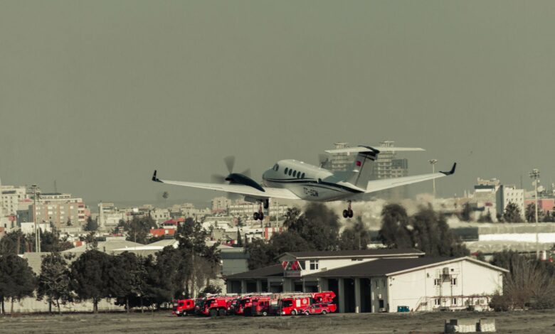 Airplane takes off over urban landscape with fire trucks ready at the fire station.