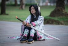 Cosplayer dressed as an anime character with a sword sitting outdoors on a sunny day.