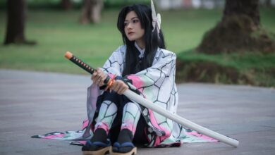 Cosplayer dressed as an anime character with a sword sitting outdoors on a sunny day.