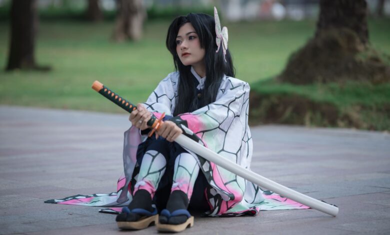 Cosplayer dressed as an anime character with a sword sitting outdoors on a sunny day.
