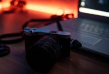 A moody composition featuring a camera and laptop on a desk with warm ambient lighting.