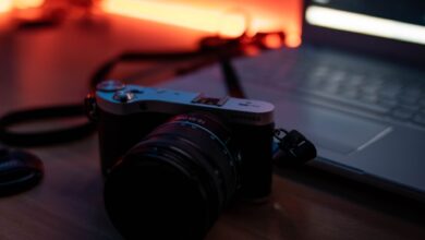 A moody composition featuring a camera and laptop on a desk with warm ambient lighting.