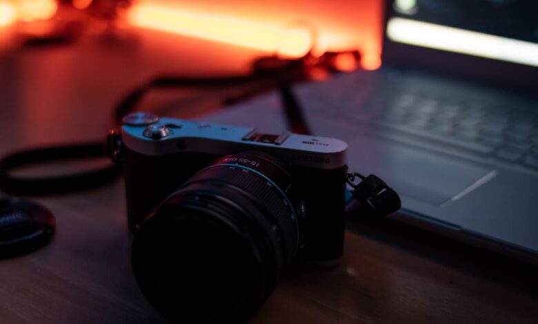 A moody composition featuring a camera and laptop on a desk with warm ambient lighting.