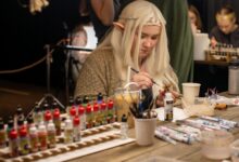 A woman cosplays as an elf while painting miniatures at an indoor convention.