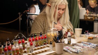 A woman cosplays as an elf while painting miniatures at an indoor convention.