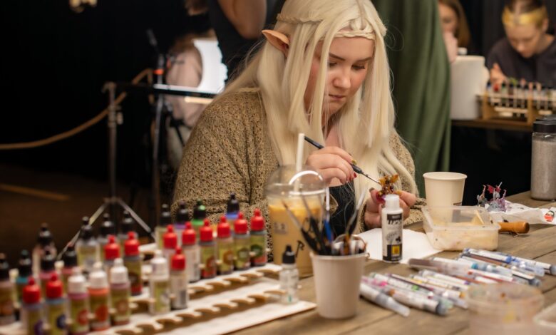 A woman cosplays as an elf while painting miniatures at an indoor convention.