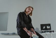 Young woman in black jacket handcuffed with cash, conceptual indoors setting.