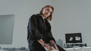 Young woman in black jacket handcuffed with cash, conceptual indoors setting.