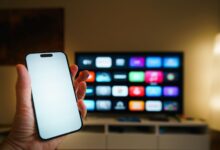 A smartphone in focus with a smart TV displaying apps in a cozy living room.