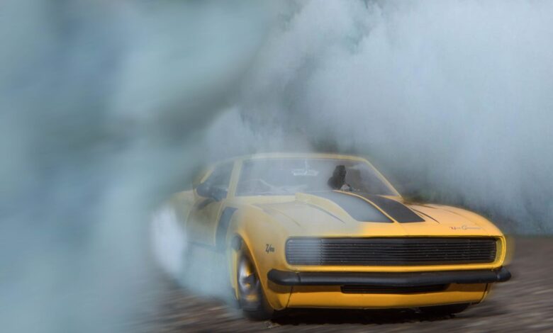 1969 Camaro drifting on pavement with smoke engulfing the car, showcasing its power.