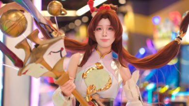 Cosplayer in elaborate costume poses in vibrant, colorful arcade environment.