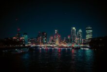 A vibrant night view of the London skyline featuring neon lights reflecting on the Thames River.