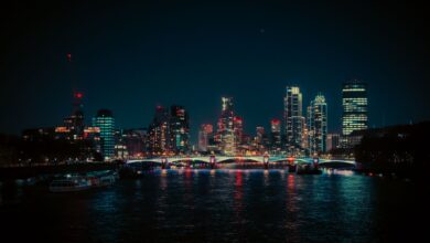 A vibrant night view of the London skyline featuring neon lights reflecting on the Thames River.