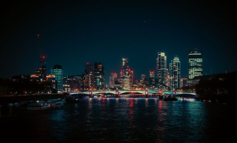 A vibrant night view of the London skyline featuring neon lights reflecting on the Thames River.