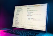 A laptop screen showing a code editor with visible programming code in a dimly lit environment.