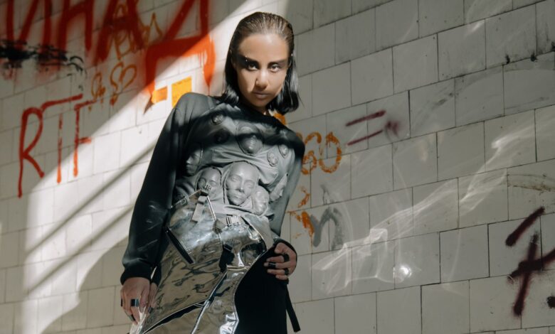 A woman posing in a futuristic outfit with graffiti in the background.