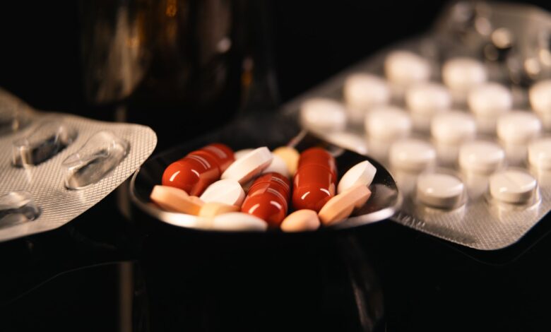 Close-up of assorted pharmaceutical pills in blister packs and a spoon on a dark background.