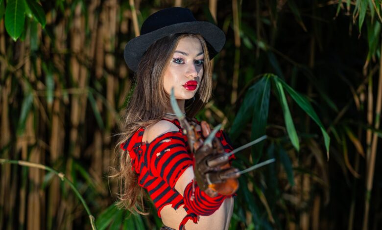 A woman in a red and black striped costume with a claw glove poses outdoors.
