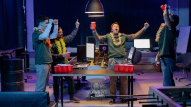 A group of friends playing beer pong indoors, celebrating with red cups and leis around their necks.