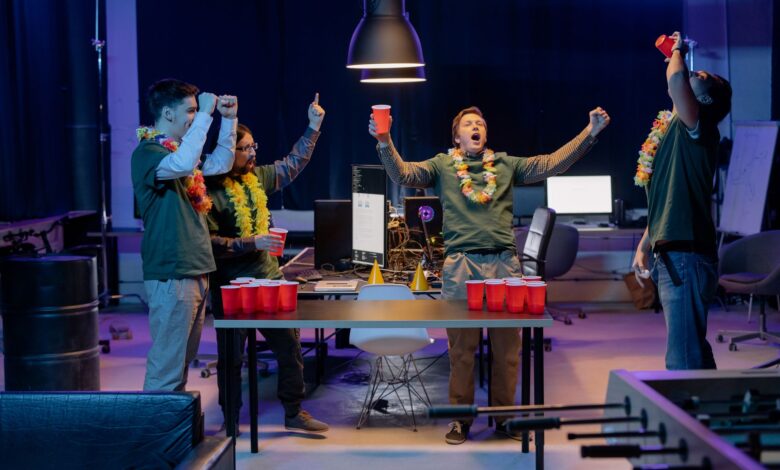 A group of friends playing beer pong indoors, celebrating with red cups and leis around their necks.