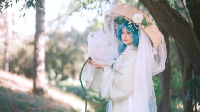 A woman in delicate cosplay attire poses outdoors with blue hair and a parasol.