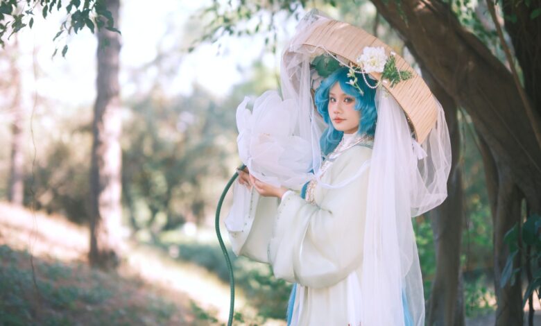 A woman in delicate cosplay attire poses outdoors with blue hair and a parasol.