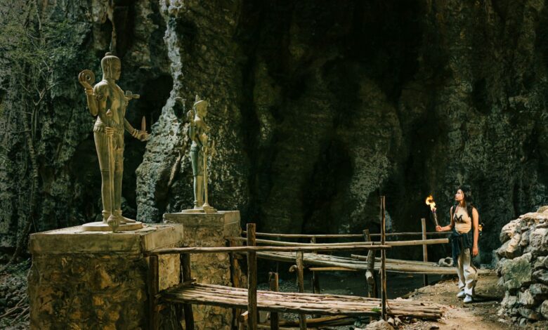 Woman with torch exploring a cave temple with ancient statues and rock formations.
