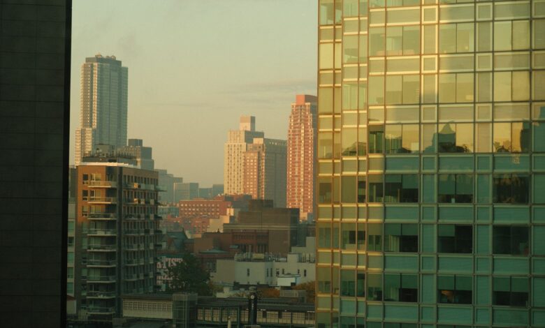 View of New York City's skyline at dawn with reflections on modern buildings.