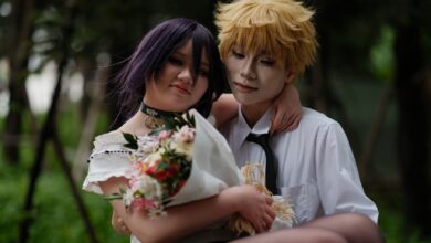A couple in anime-style cosplay poses outdoors, with a bouquet and a warm embrace.