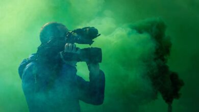 A professional cameraman captures footage surrounded by striking green smoke, highlighting filmmaking elements.