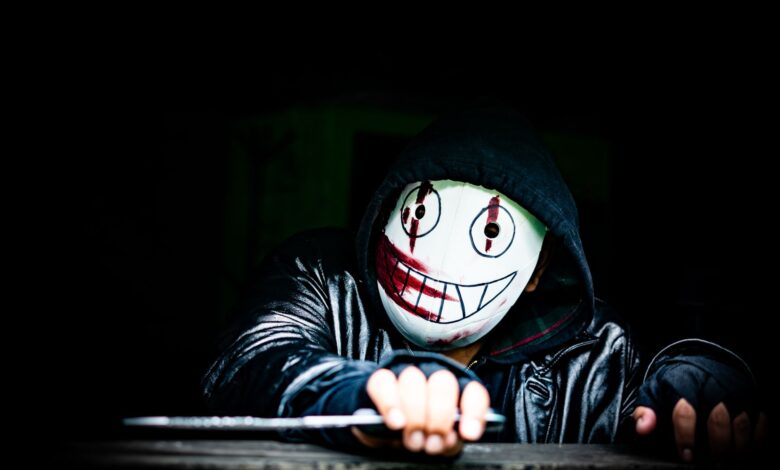 A mysterious figure wearing a creepy smiling mask in a dark setting, creating an eerie atmosphere.