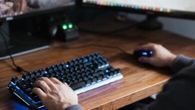 High angle crop male in casual clothes sitting at desk and browsing contemporary computer while typing on backlit keyboard and using mouse
