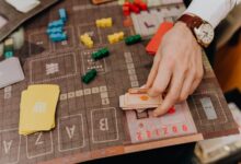 Close-up of a hand playing a board game with cards and colorful pawns.