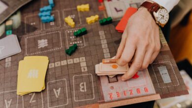 Close-up of a hand playing a board game with cards and colorful pawns.