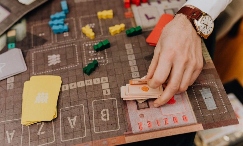 Close-up of a hand playing a board game with cards and colorful pawns.