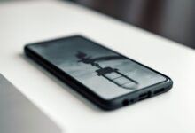 Close-up of a smartphone displaying a blurred image, placed on a desk beside a laptop.
