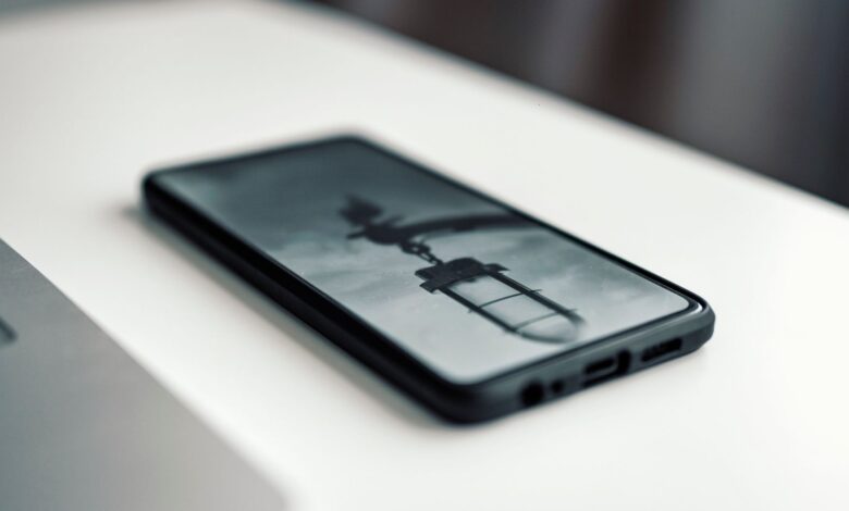 Close-up of a smartphone displaying a blurred image, placed on a desk beside a laptop.