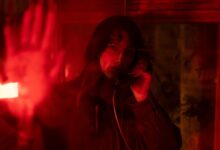 A woman in a telephone booth, surrounded by dramatic red lighting.