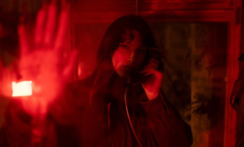 A woman in a telephone booth, surrounded by dramatic red lighting.