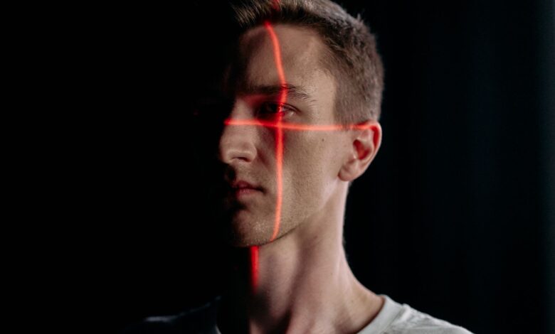 Studio portrait of a man with a laser grid pattern for facial recognition on a black background.