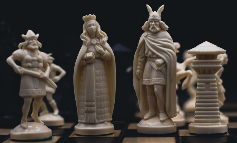 Detailed close-up of intricately carved chess pieces on a chessboard, evoking a medieval theme.