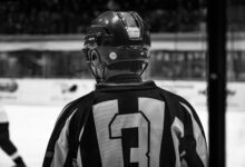 Black and white photo of ice hockey player in helmet from behind, captured during a match.